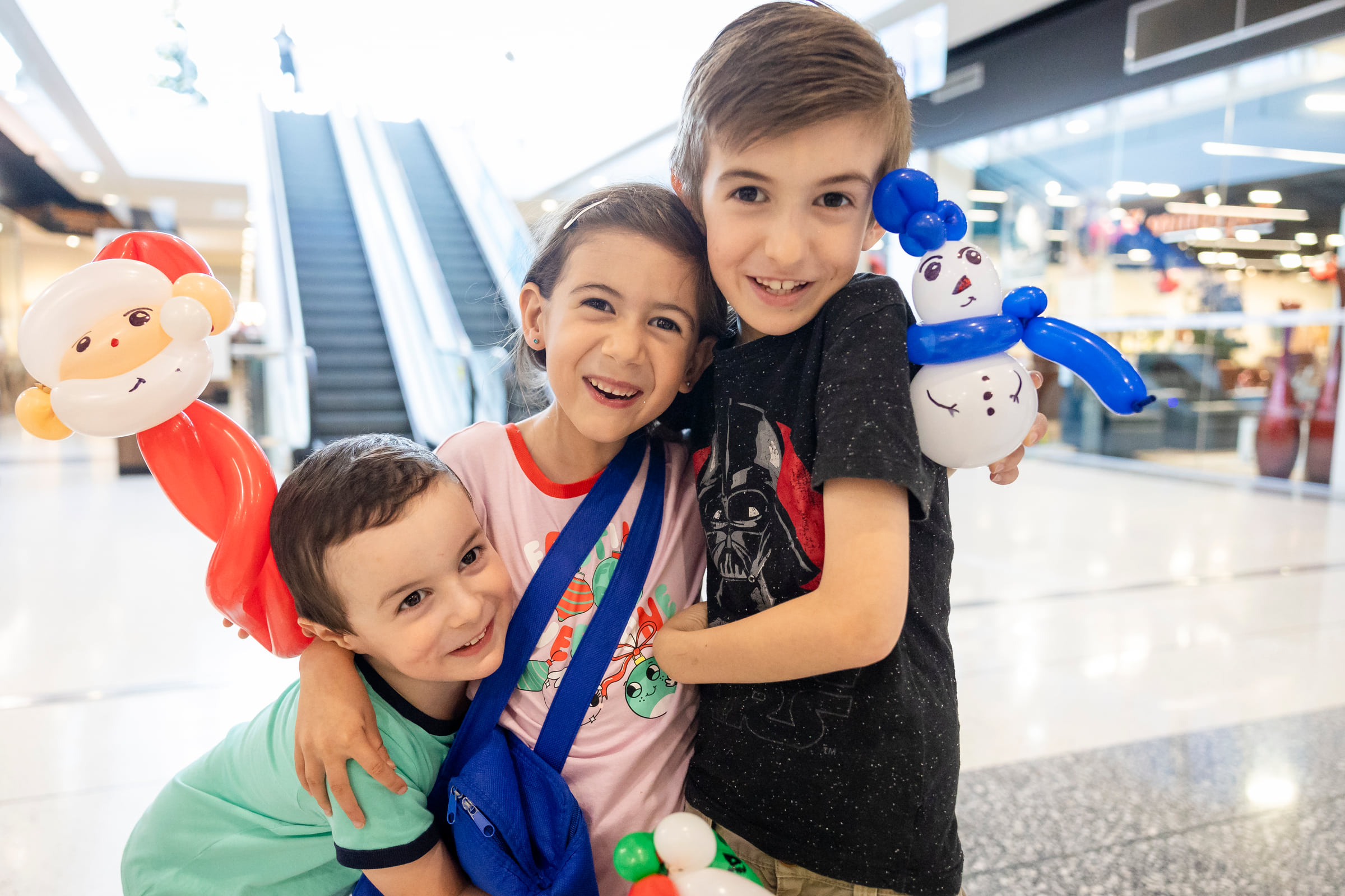 Three children smiling together with Santa and snowman balloons