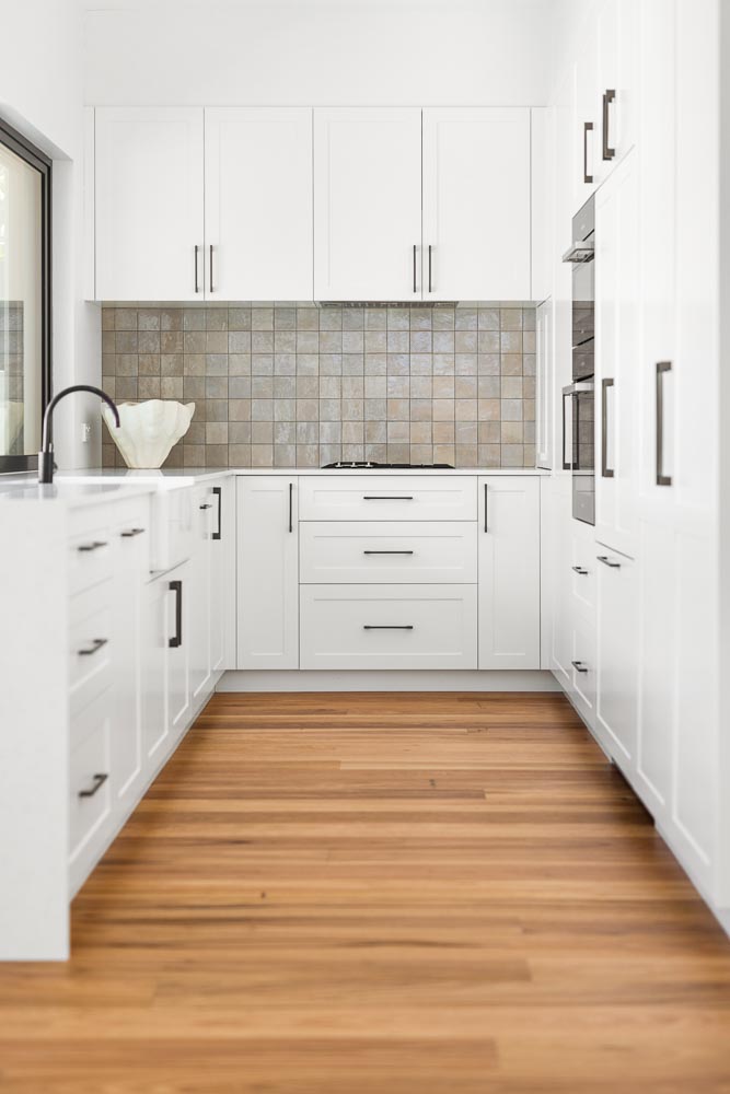 White kitchen joinery, tiled splashback and warm timber flooring