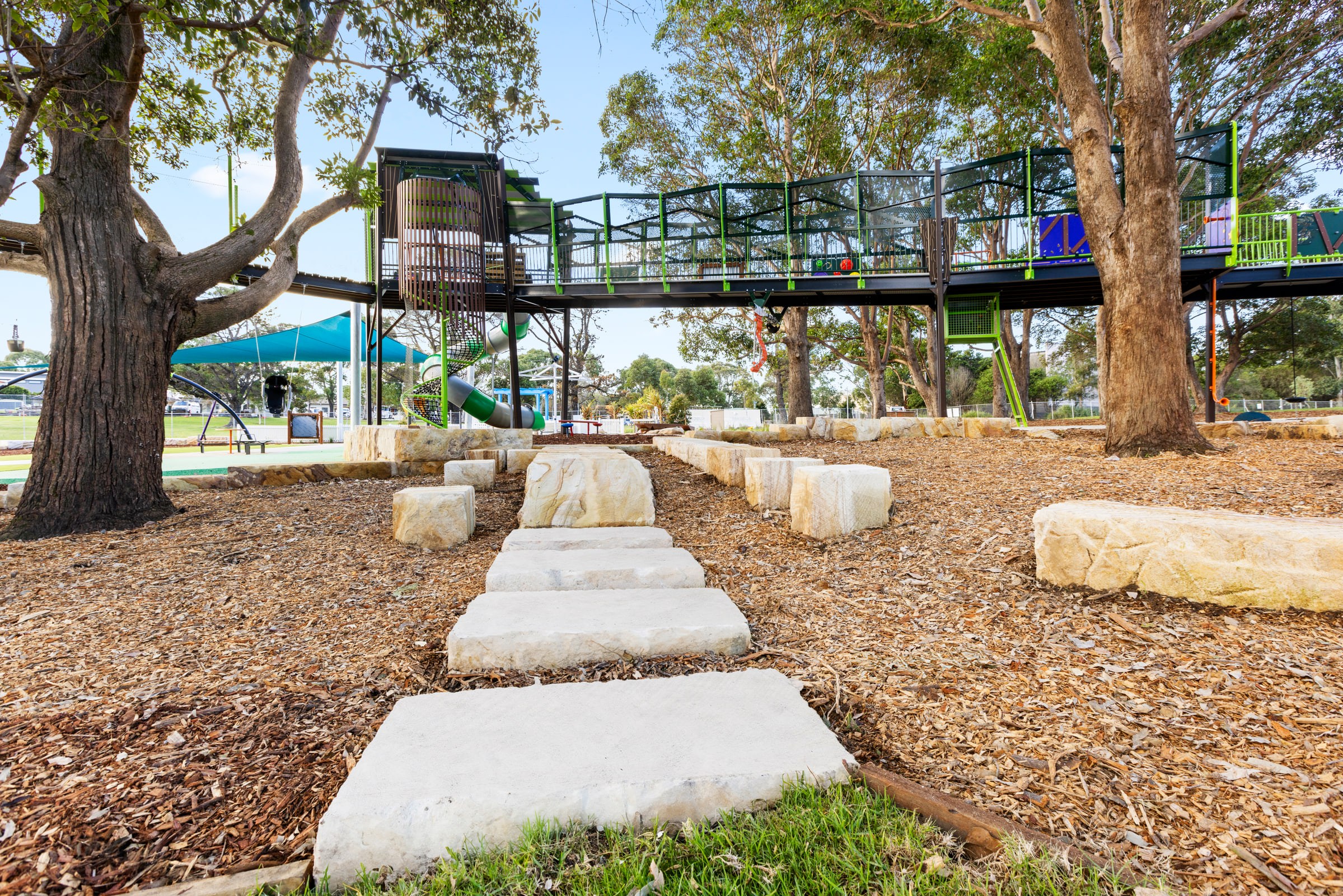 Tall green and brown play tower with a curved tube slide behind a sandstone retaining wall