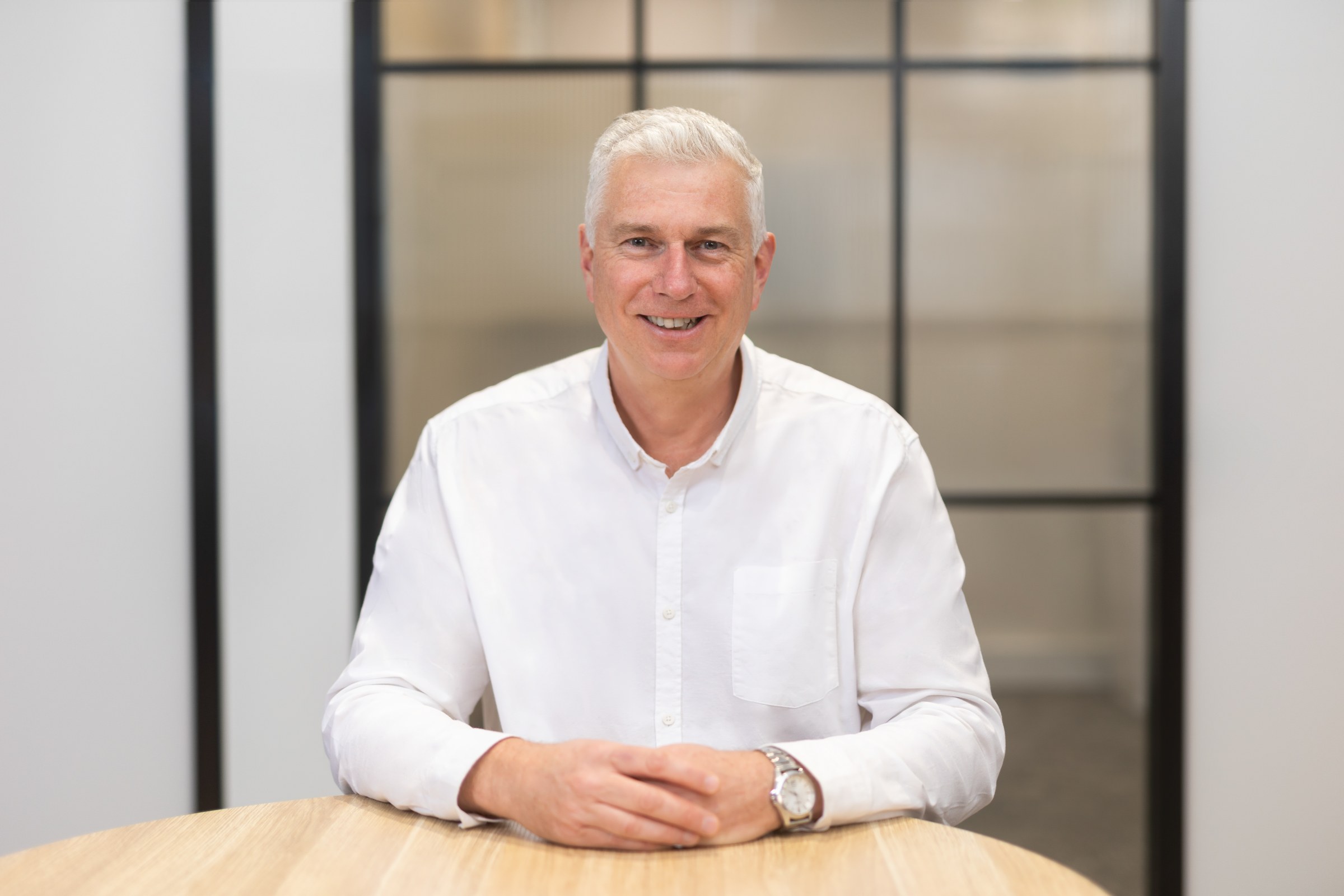 Plan Project Management team member in a white shirt seated at a timber table