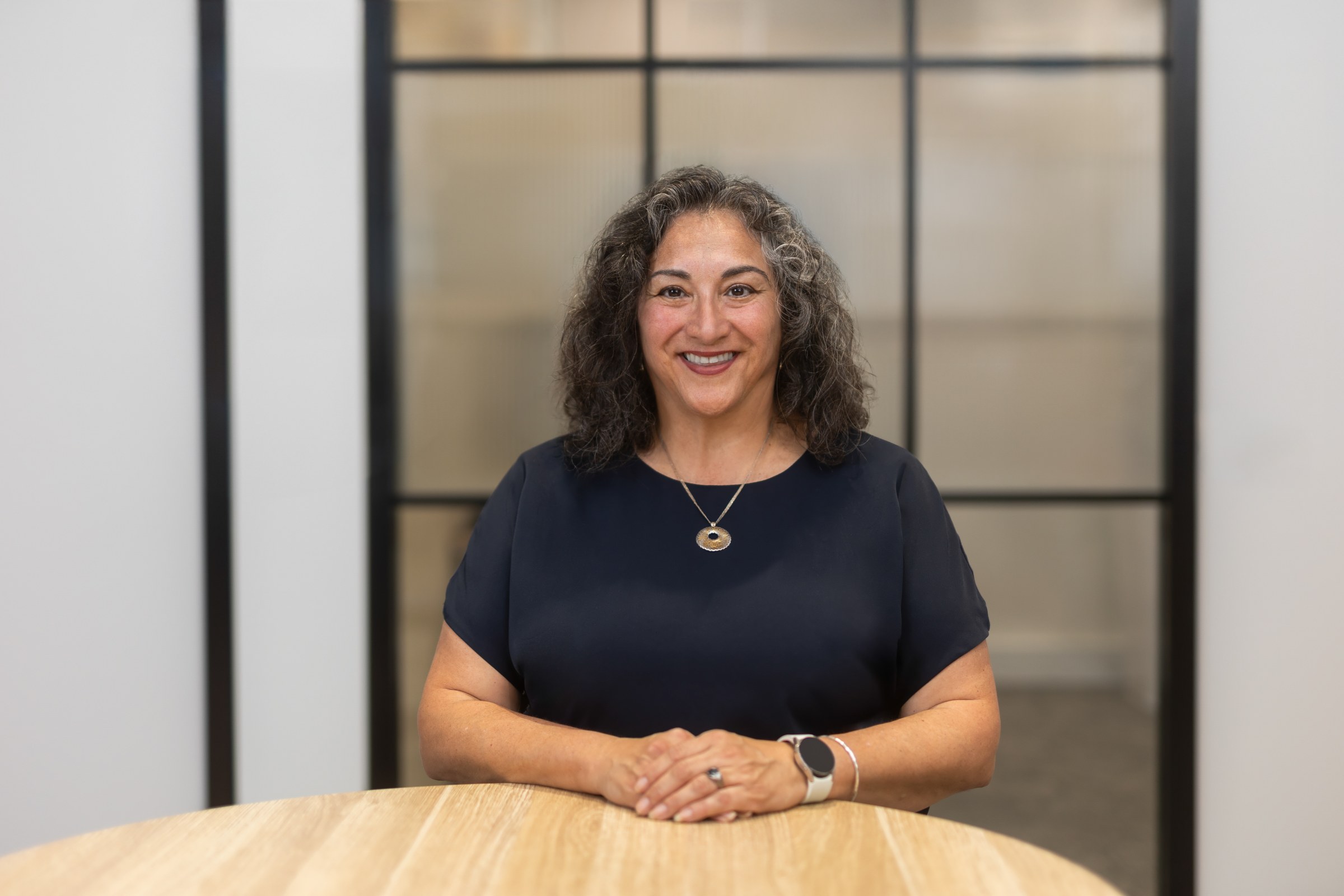 Plan Project Management team member with curly hair wearing a navy top at a timber table